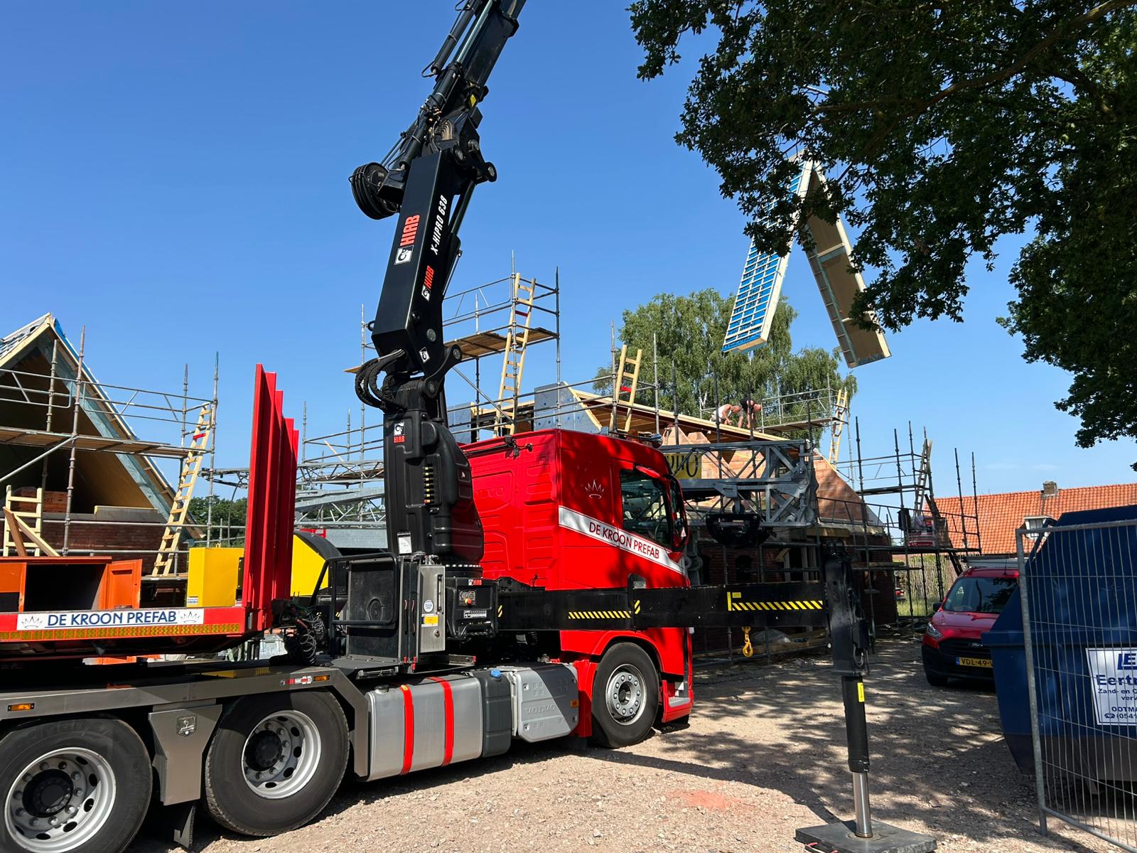 achter de bomen tilt een kraan prefab dakelementen