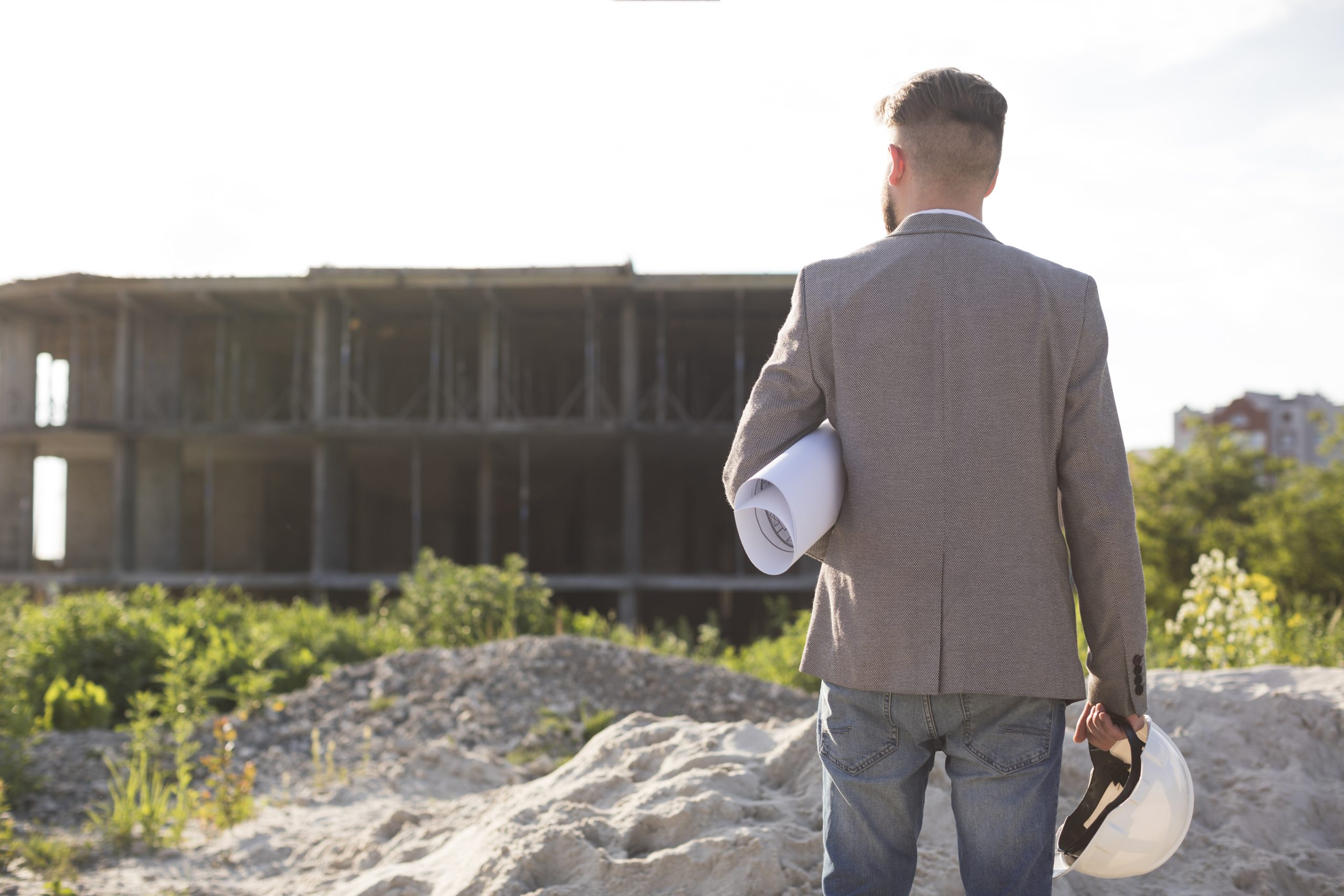 rear view male architecture holding blueprint hard hat looking construction site scaled